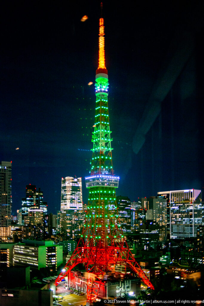 Centered night view of Tokyo Tower with green shaft, red base, and orange antenna.