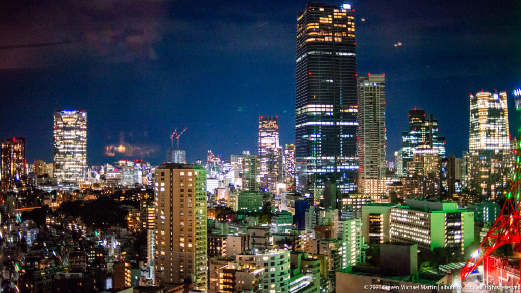 Night skyline of Tokyo high-rises and cranes with part of Tokyo Tower at lower right.