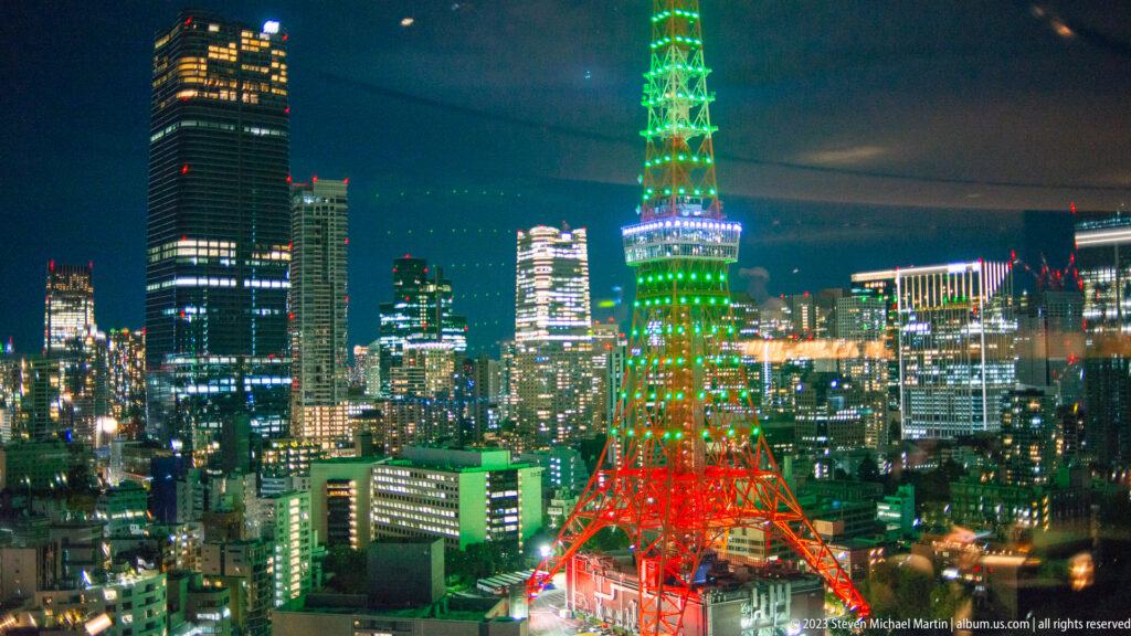 Tokyo Tower illuminated green and red above a night skyline with window reflections.