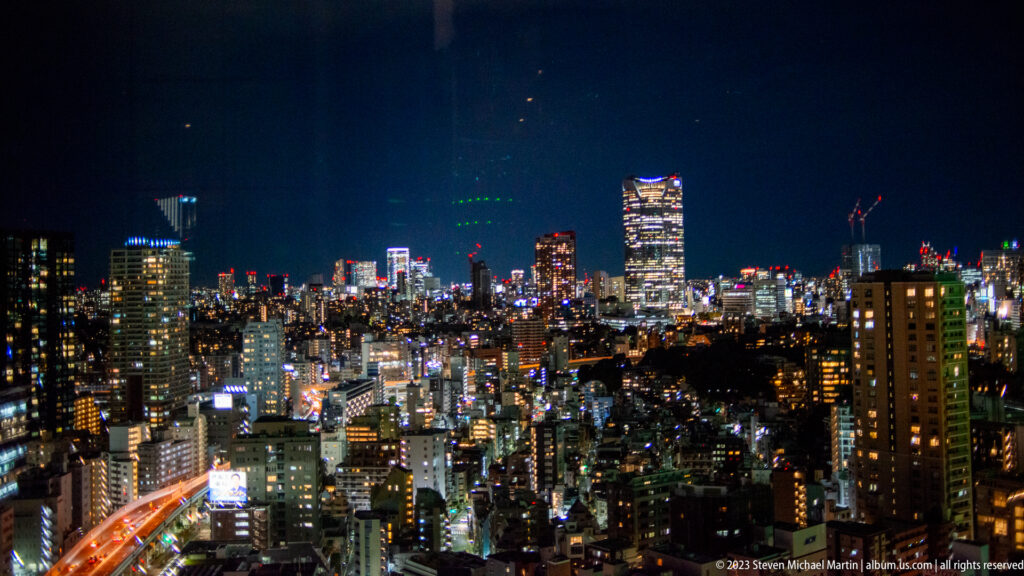Wide Tokyo night skyline with dense buildings and an orange curving expressway.