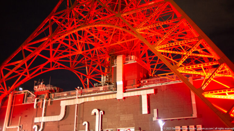Red illuminated Tokyo Tower lattice arches above base buildings and service equipment.