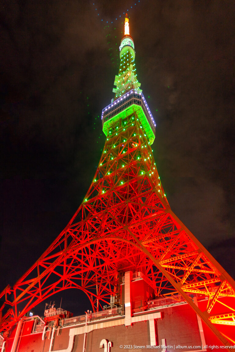 Centered low-angle view of Tokyo Tower glowing red, green, blue, and orange.