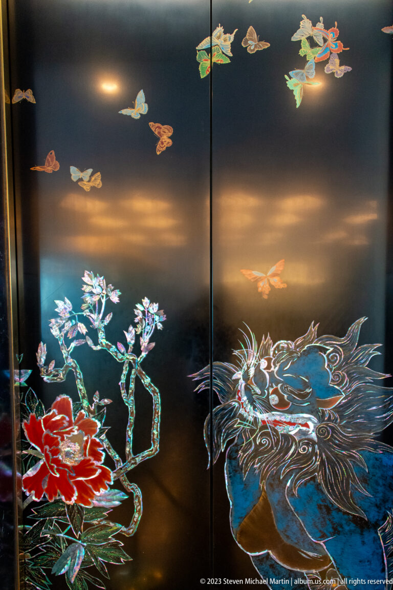 Black decorative panel with flying birds, flowering branches, and a large blue wave-like motif.