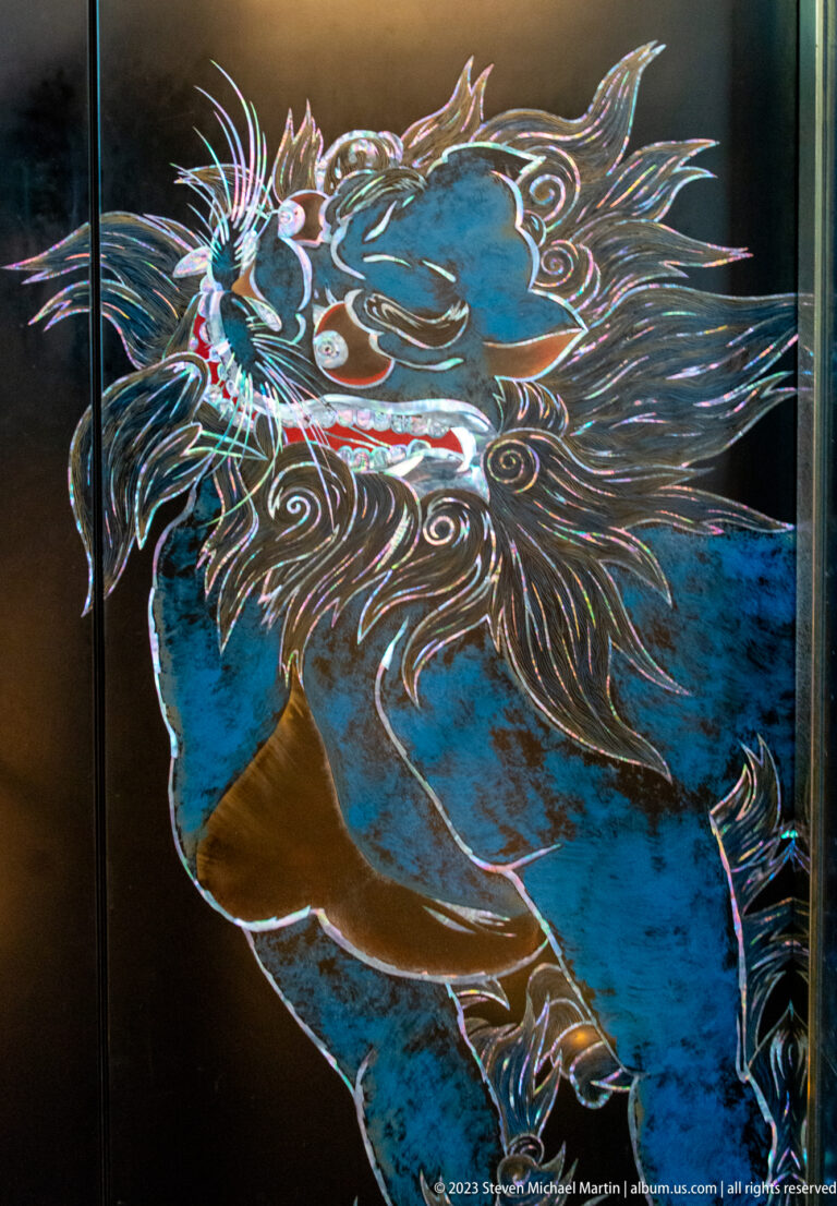Close-up of a blue swirling animal-like figure with iridescent outlines on a black panel.