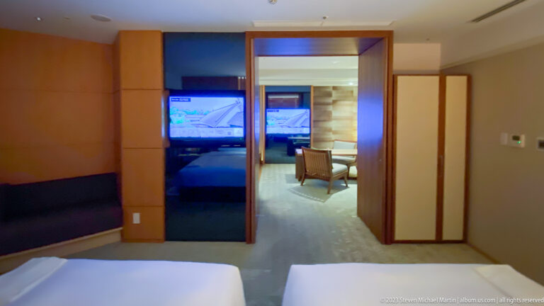 Hotel suite with sliding wood partitions opening from the bed toward adjoining rooms.