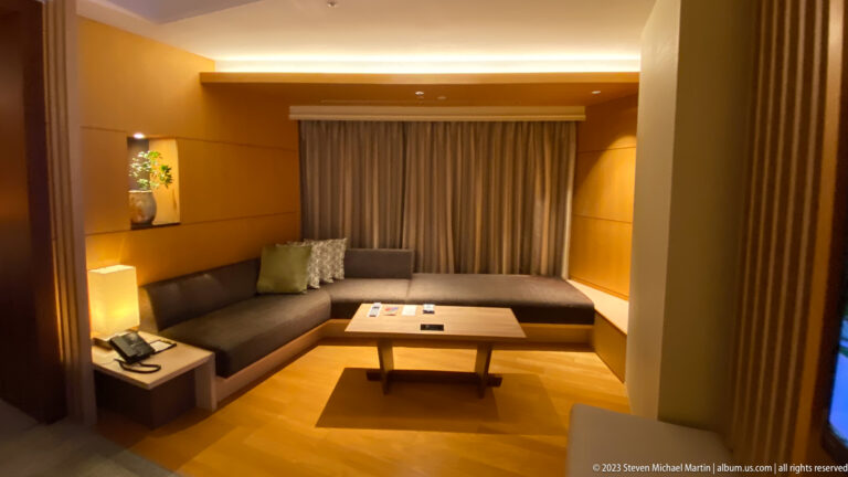 Hotel living area with built-in sectional sofa, low coffee table, and curtained window.
