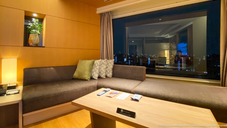 Built-in sofa and wood coffee table beside a large window with nighttime city lights.