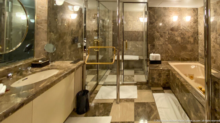 Marble bathroom with long vanity, glass shower enclosure, and deep soaking tub.