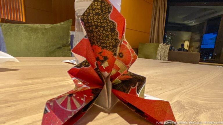 Standing folded-paper figure in red, black, white, and gold patterns on a table.