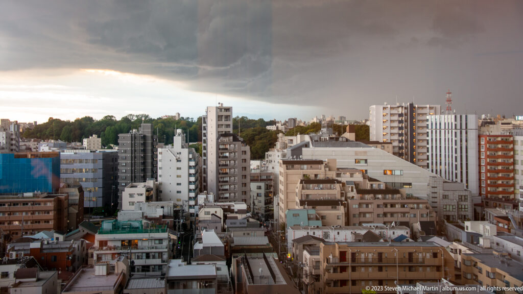 Elevated Tokyo cityscape of apartment blocks and rooftops beneath dark storm clouds.
