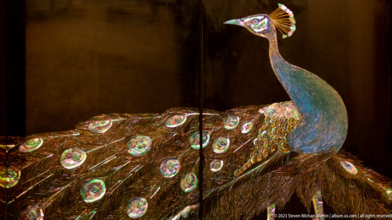 Iridescent peacock sculpture in profile with jeweled eye-feather motifs across its tail.