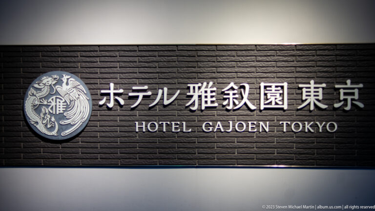 Illuminated Hotel Gajoen Tokyo sign in Japanese and English on a dark brick wall.