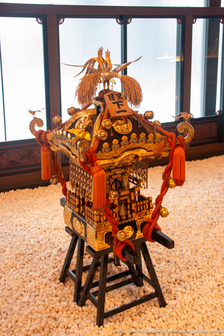 Three-quarter view of a gilded mikoshi with red tassels, phoenix finial, and black carrying poles.