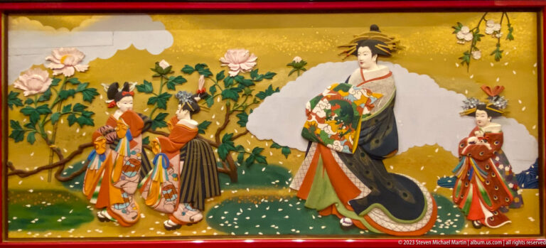 Central woman in formal kimono attended by women and children among peonies and flowering cherry branches.
