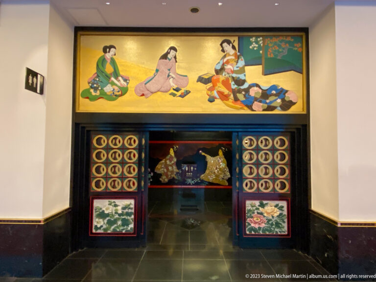 Ornamental doorway framed by floral panels, circular motifs, and a narrative scene of women above.
