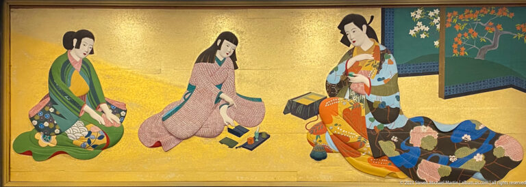 Three seated women in kimono examine folded textiles beside a flowering screen on a gold ground.