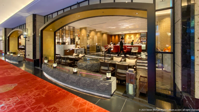Arched restaurant entrance with black stone counters, metal screens, warm lighting, and red carpet.