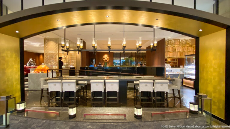 Symmetrical bar with high stools beneath a gold-toned arch and warm pendant lighting.