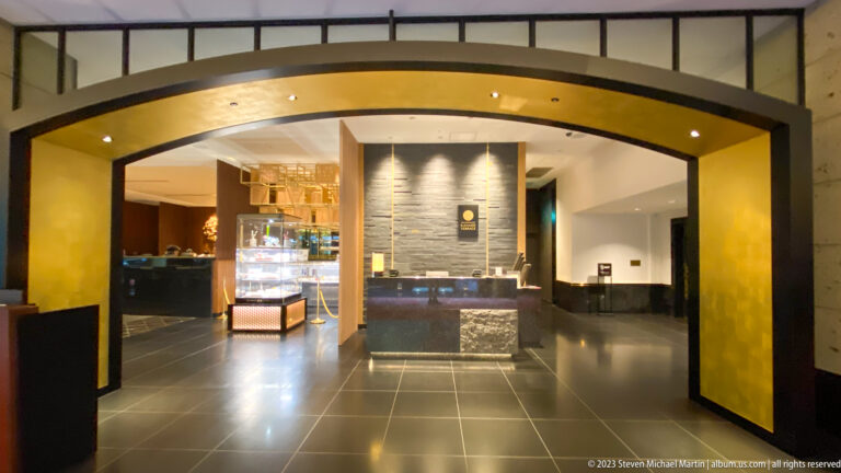 Gold-framed arch opening onto a reception desk, illuminated display case, and dark tiled floor.