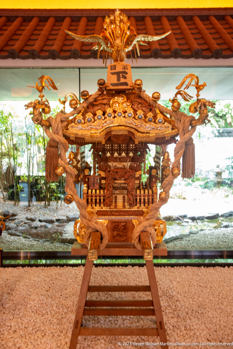 Carved wooden mikoshi with gilded fittings, tassels, phoenix finial, and projecting poles.