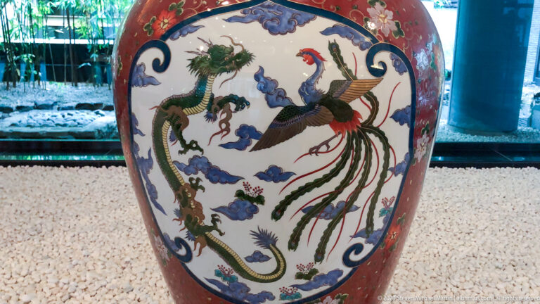Dragon and long-tailed phoenix face each other amid blue clouds and floral borders on a ceramic jar.
