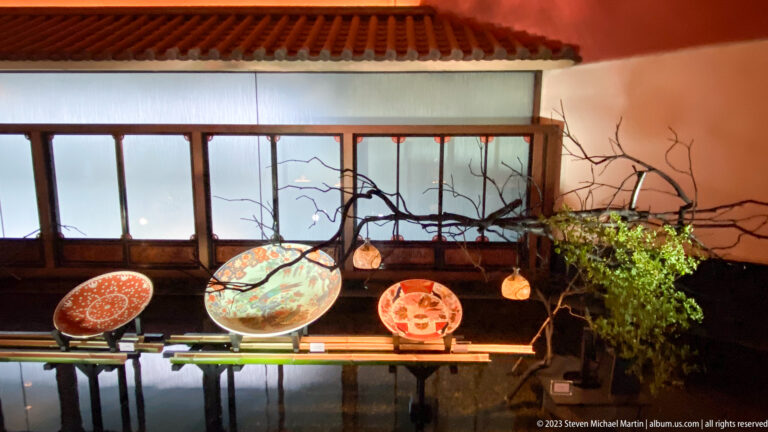 Decorated ceramic plates arranged with bare branches, small vessels, and green plants on a low shelf.