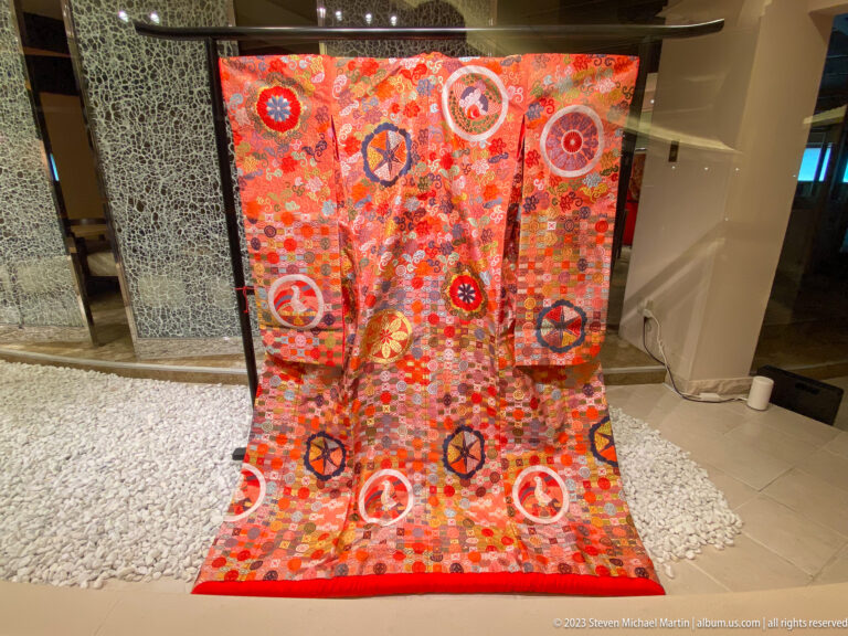 Formal red kimono displayed upright with circular medallions, flowers, and geometric patterns.