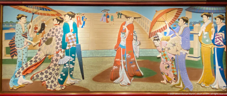 Women in patterned kimono walk in procession across a promenade carrying broad parasols.