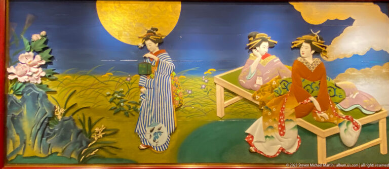 Three women in kimono rest near tall grasses beneath a large golden full moon.