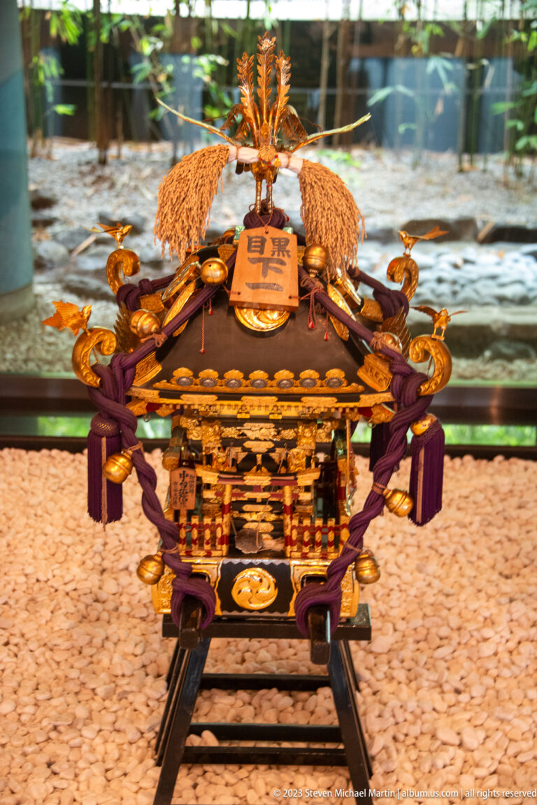 Compact front-facing mikoshi with purple cords, gilded details, phoenix finial, and carrying poles.