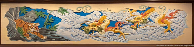 Two tigers confront several dragons emerging through swirling clouds beside rocks and bamboo.