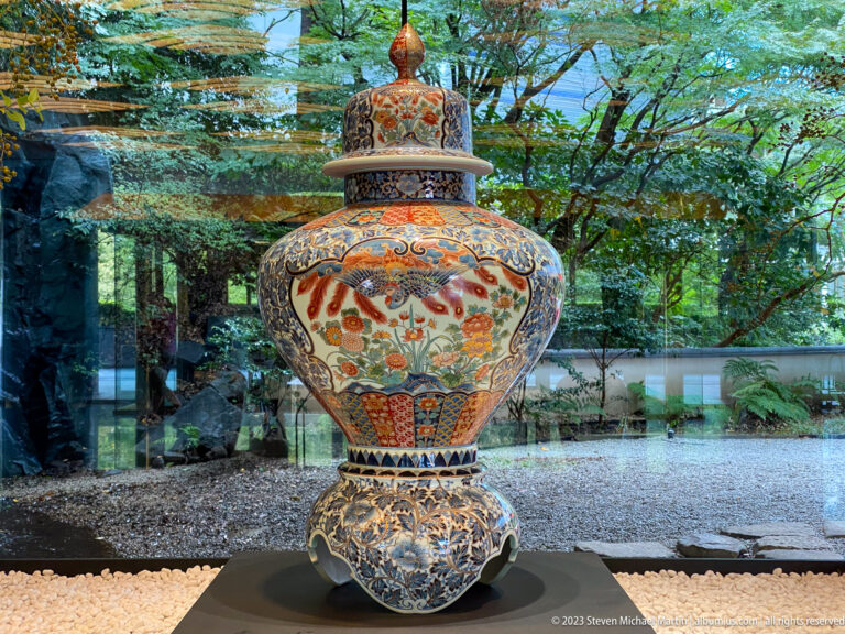 Large polychrome lidded jar with birds and floral decoration displayed before a garden window.