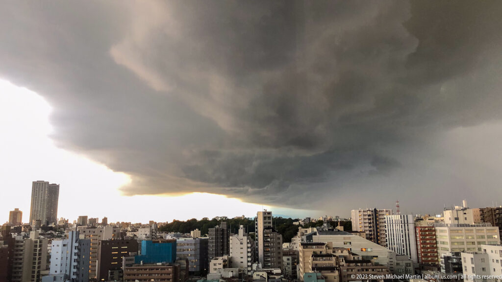 Dark storm front advancing over Tokyo high-rises with bright light remaining at the horizon.