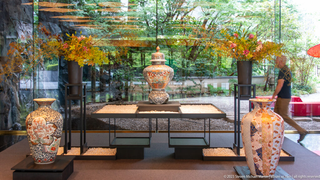 Large patterned ceramic vases displayed on platforms before a glass wall and garden.