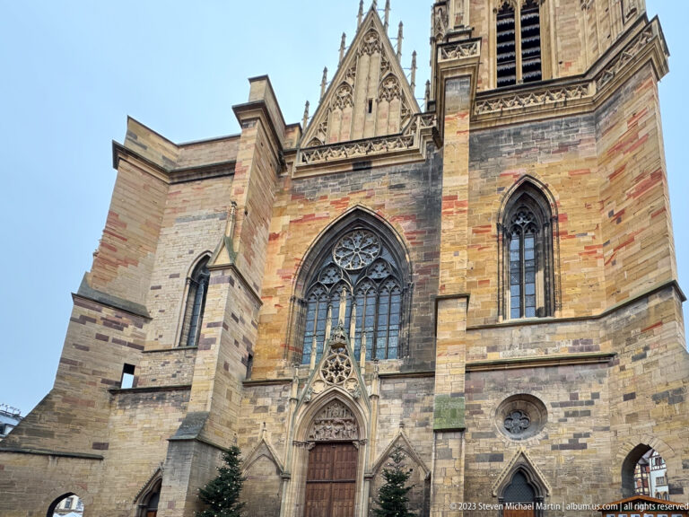 Close upward view of Gothic sandstone portal, large traceried window, narrow lancets, and steep gable.