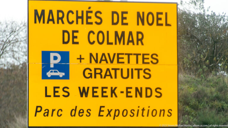Yellow sign for Colmar Christmas markets advertising parking and free weekend shuttles at Parc des Expositions.
