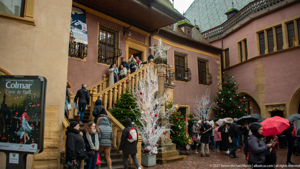 Visitors climb a stone staircase between Christmas trees and white branch decorations with gold ornaments.