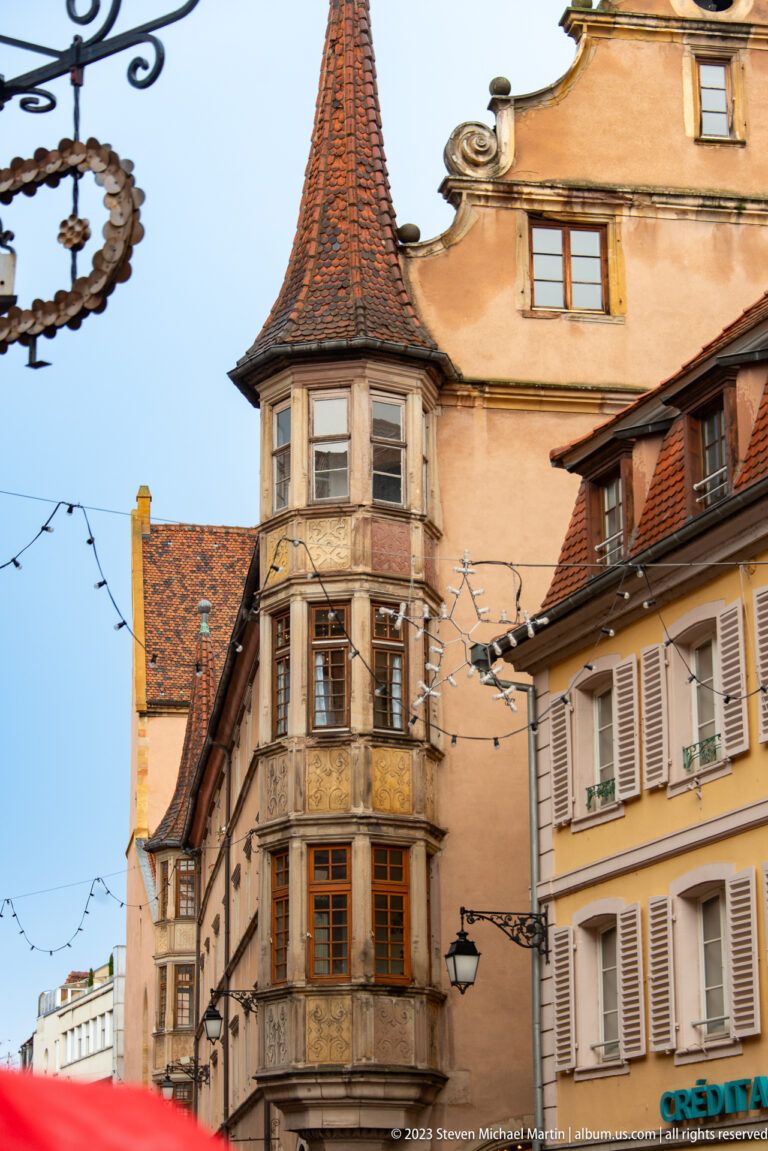 Multi-story polygonal stone bay with carved window surrounds and a steep tiled cap on a historic Colmar house.