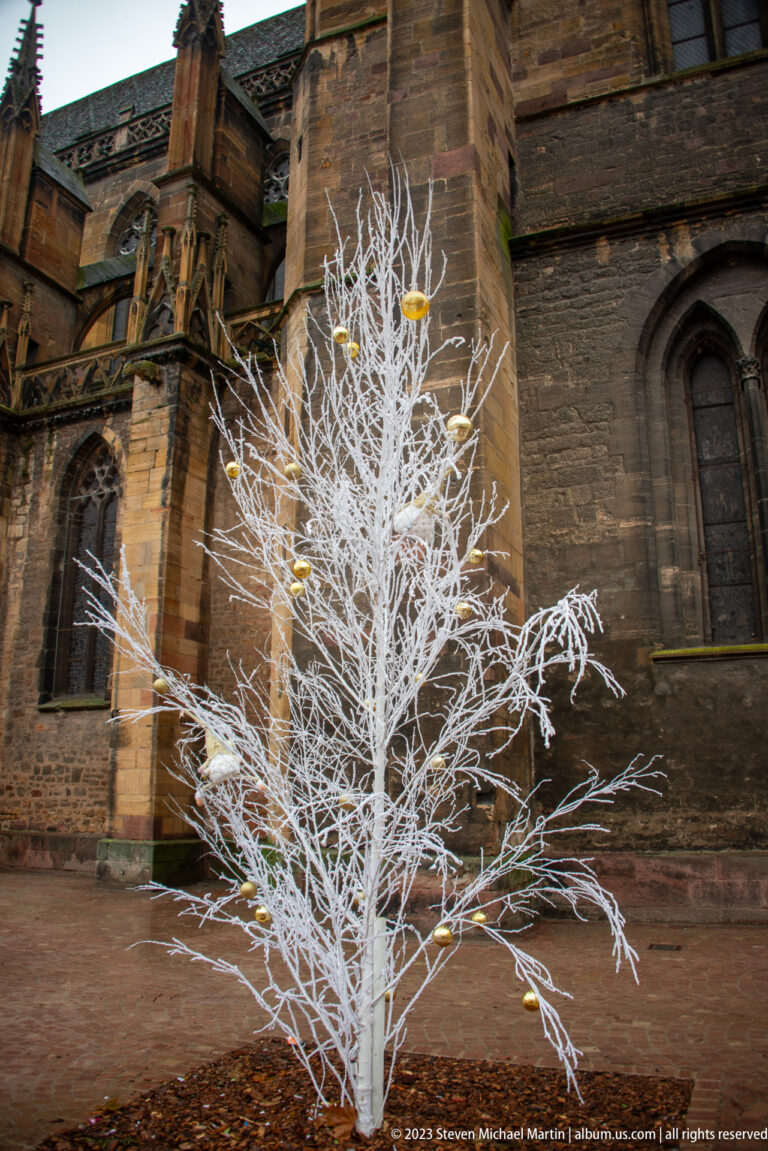White decorative tree with gold ornaments standing against dark Gothic church walls and pointed-arch windows.
