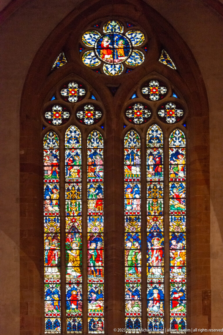 Large multicolored Gothic stained-glass window with tall lancets, circular upper tracery, and many figurative panels.