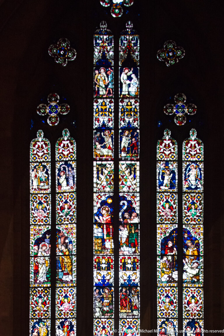 Three groups of bright figurative stained-glass windows glowing against a dark Gothic church interior.