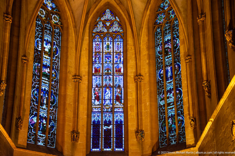 Three tall figurative stained-glass windows set in pointed Gothic arches within warm stone walls.