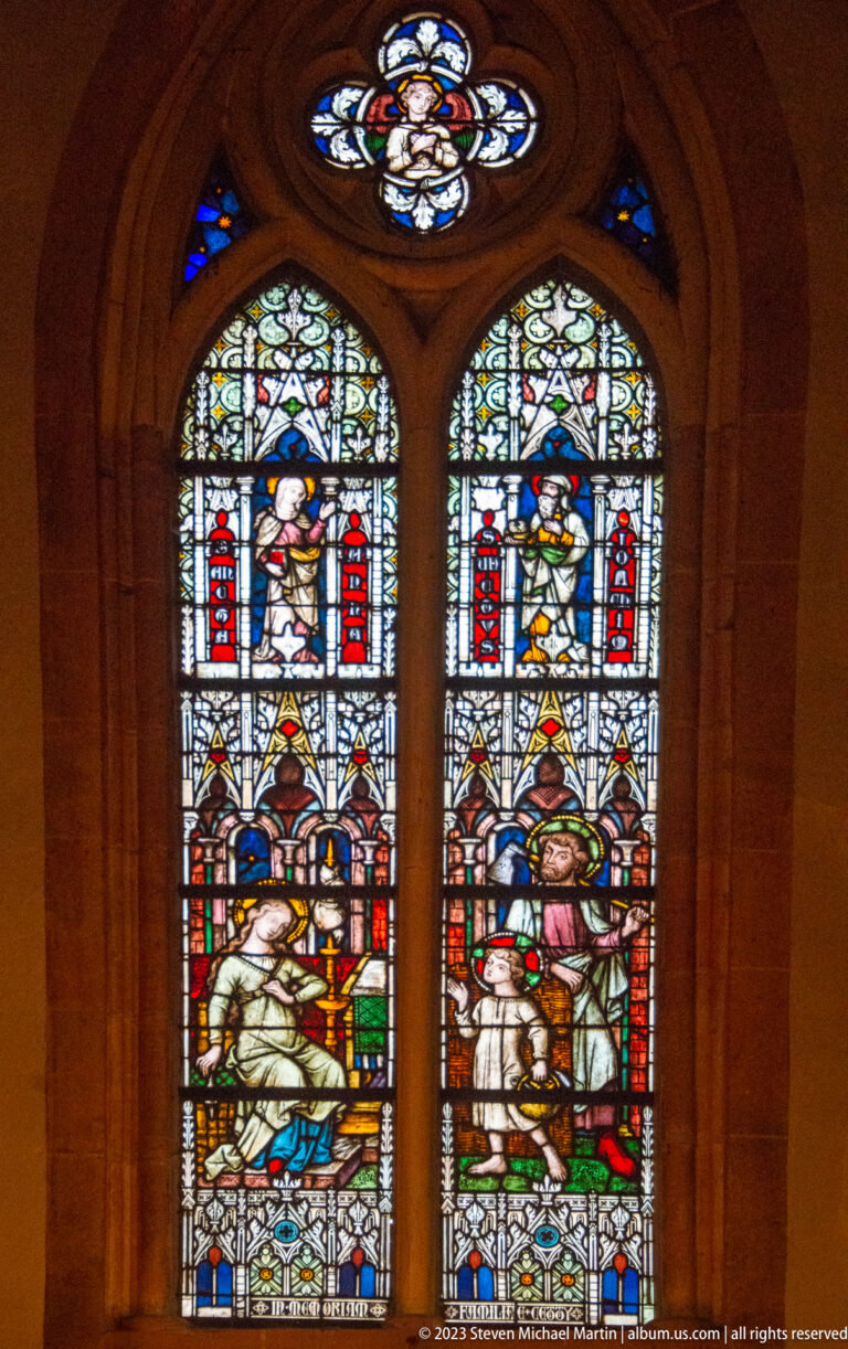 Two richly colored figurative stained-glass lancets beneath a small circular quatrefoil-style light.