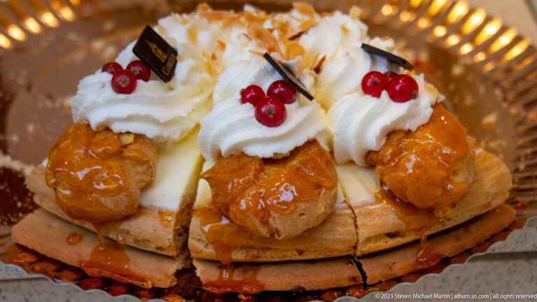 Large round pastry topped with glazed choux puffs, whipped cream, red berries, almonds, and chocolate decorations.