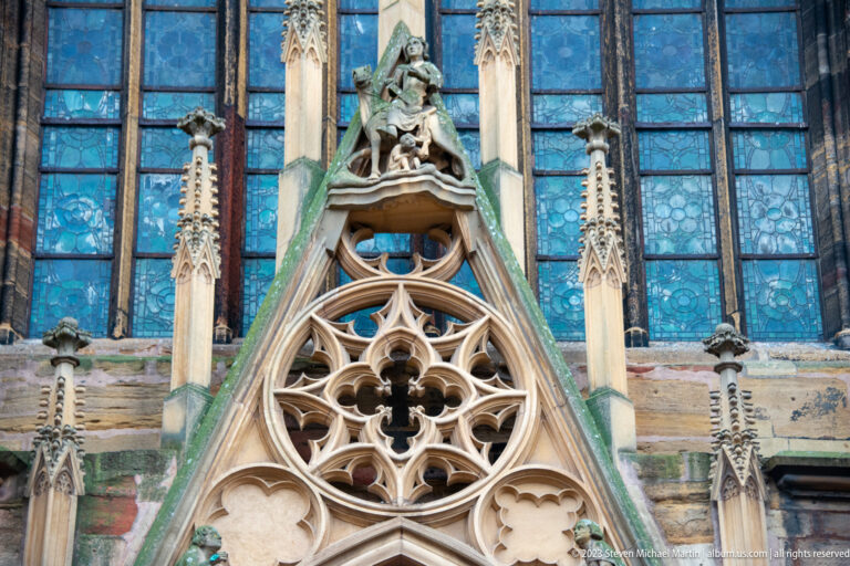 Gothic stone tracery, pinnacles, blue windows, and a sculpted figure on Saint Martin's Church in Colmar.