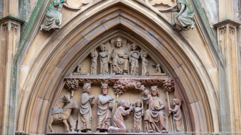 Pointed Gothic doorway with two tiers of carved stone figures filling the tympanum and lintel area.