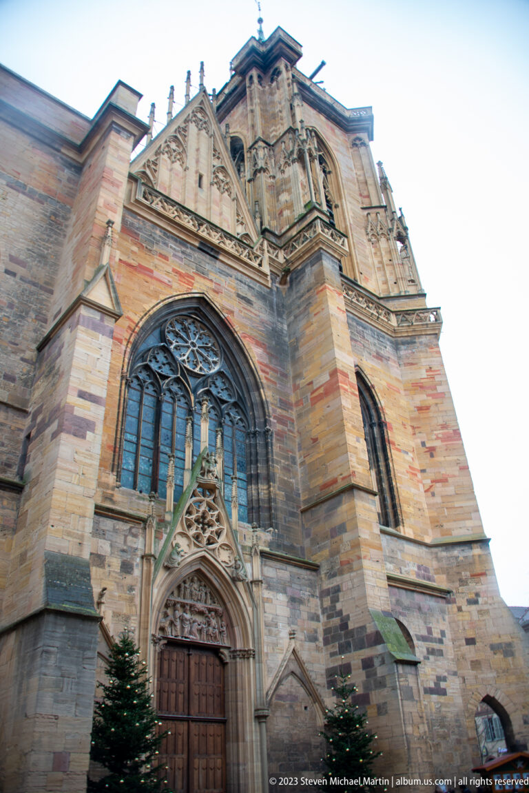 Upward view of Saint Martin's Church façade with sandstone walls, pointed window, sculpted doorway, and steep gable.