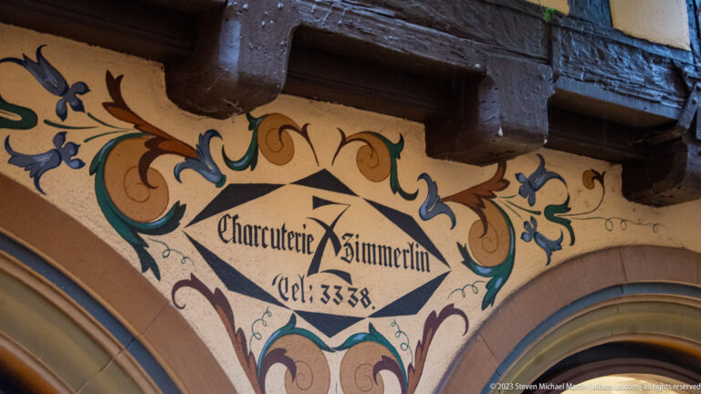 Painted Charcuterie Zimmerlin inscription with scrolling ornament beneath dark timber beams on a historic façade.