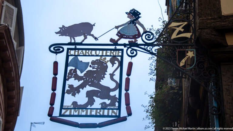 Decorative wrought-iron hanging sign for Charcuterie Zimmerlin with butcher-themed silhouettes and ornamental scrollwork.