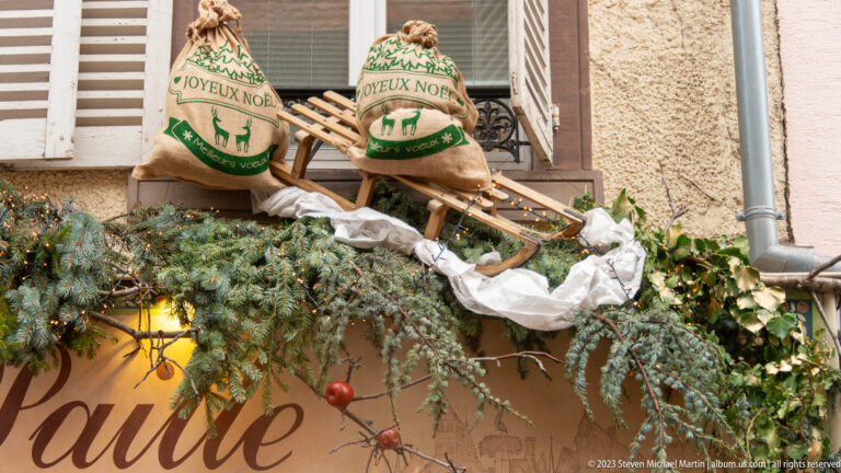 Burlap holiday sacks and a wooden sled rest among evergreen branches, ivy, white fabric, and red ornaments.
